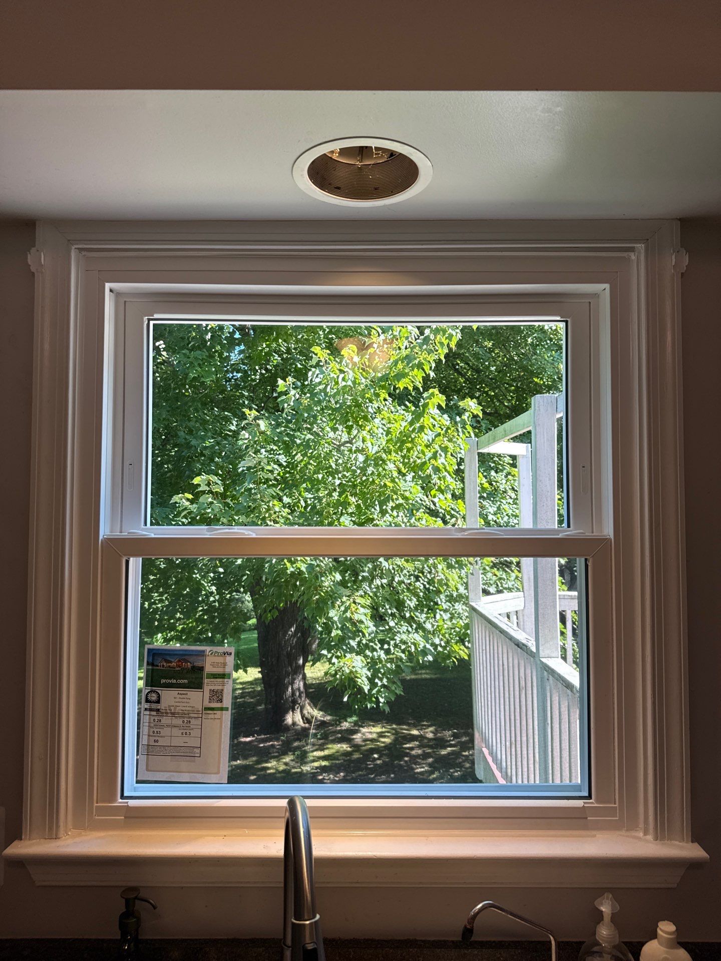 Kitchen sink window before and after replacement with a white ProVia Aspect double-hung window in Sykesville, Maryland
